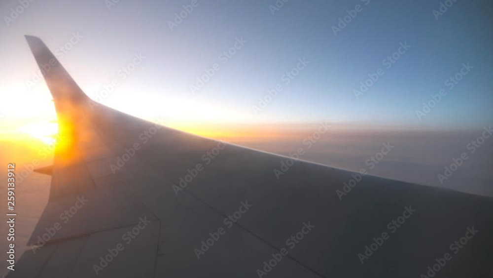 View from airplane window to sunrise or sunset. Wing of plane flying above the clouds with sun light. Aircraft flight at sky. Concept of traveling by air. Trip by airliner with beautiful background View from airplane window to sunrise or sunset. Wing of plane flying above the clouds with sun light. Aircraft flight at sky. Concept of traveling by air. Trip by airliner with beautiful background