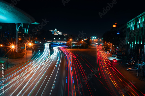 Georgia, Tbilisi - 05.02.2019. - Car light traces speeding on the highway beside Public Service Hall. presidental Palace in the background - Night photo photo