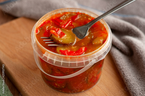 Salad of vegetables and spices in the package. Spicy food in the form of lecho from cucumbers, tomatoes, peppers and spices. Vegetable salad in plastic packaging on a cutting board. photo