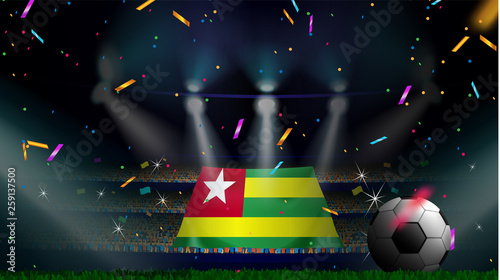 Fans hold the flag of Togo among silhouette of crowd audience in soccer stadium with confetti to celebrate football game. Concept design for football result template