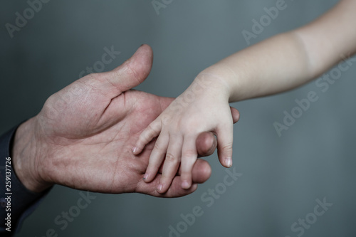 Closeup senior man and baby girl holding hands together on dark background