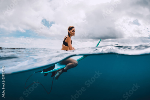Attractive young surf girl sit at surfboard in blue ocean