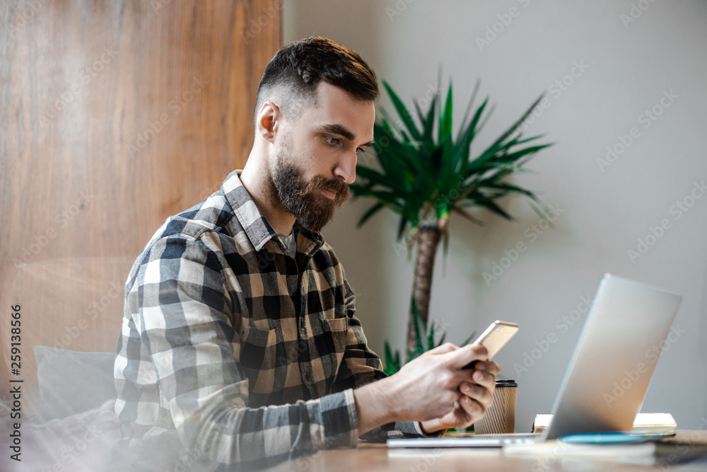 Young hipster modern businessman working on laptop at his modern office interior desk near windows, enjoying coffee and doing his freelance job. Technology and smart working process concept