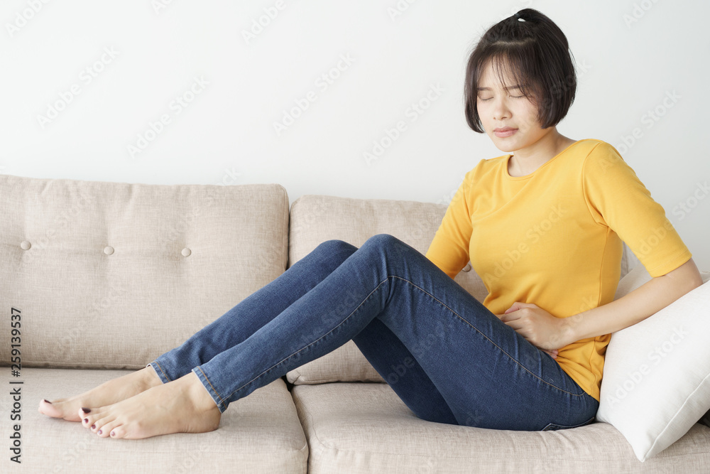 Young asian woman sit on sofa in the living room. she having painful stomachache.