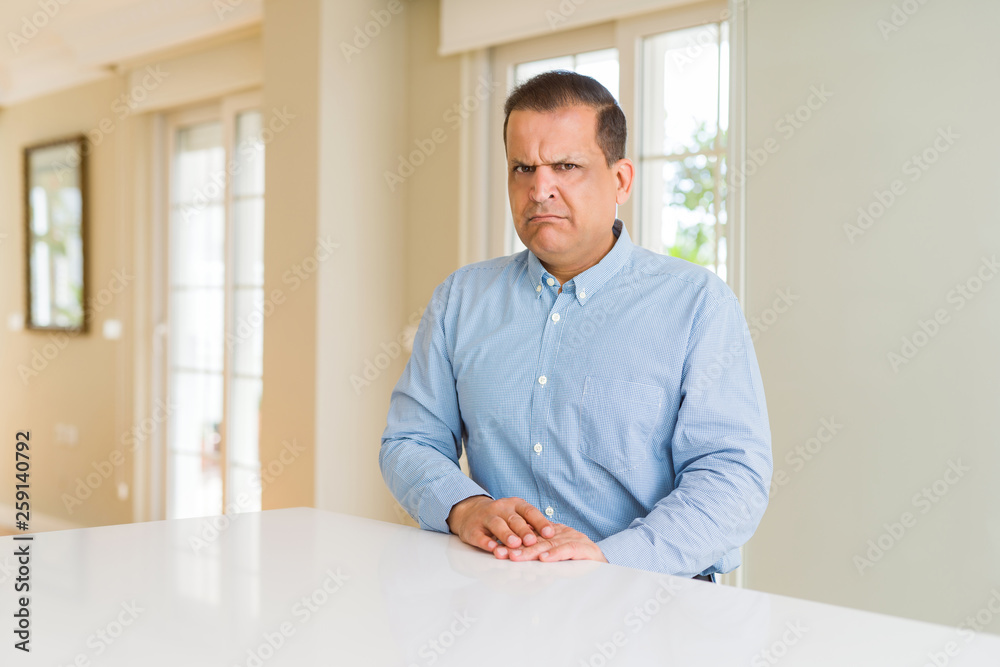 Middle age man sitting at home skeptic and nervous, frowning upset because of problem. Negative person.