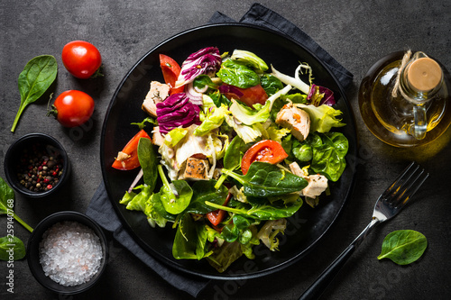 Fotografia Green salad with chicken and vegetables on black.