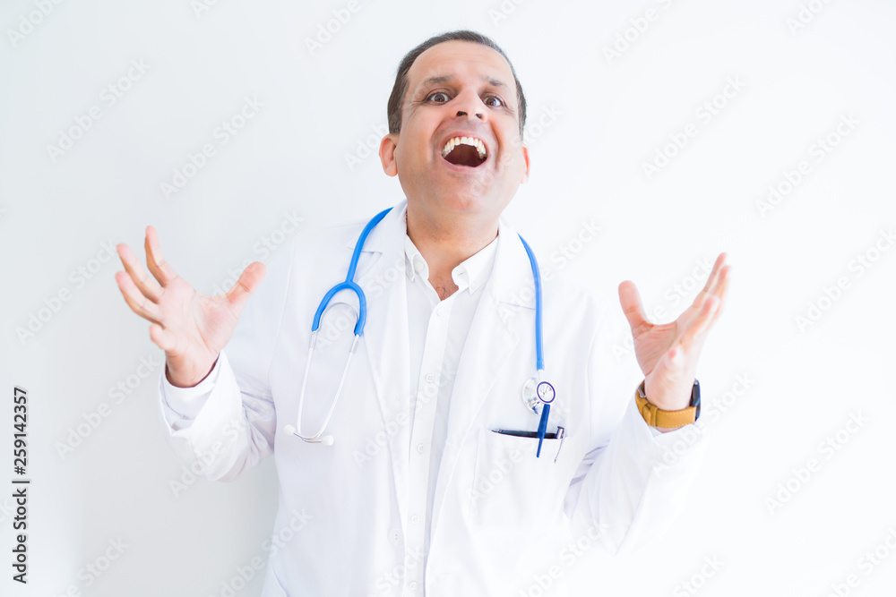 Middle age doctor man wearing stethoscope and medical coat over white background celebrating crazy and amazed for success with arms raised and open eyes screaming excited. Winner concept Middle age doctor man wearing stethoscope and medical coat over white background celebrating crazy and amazed for success with arms raised and open eyes screaming excited. Winner concept