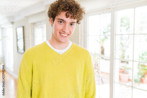 Young handsome man wearing yellow sweater at home with a happy and cool smile on face. Lucky person.