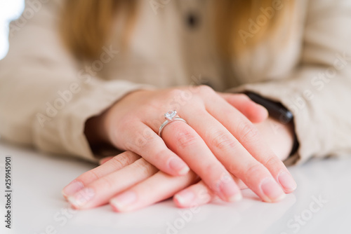 Close up of woman finger showing engagement ring with hands on each other over white table