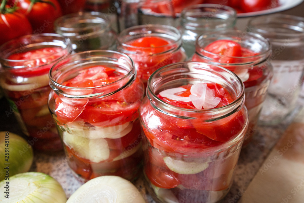 Canning fresh tomatoes with onions in jelly marinade. Woman hands putting red ripe tomato slices and onion rings in jars. Basil, parsley leaves on top of onions. Vegetable salads for winter Canning fresh tomatoes with onions in jelly marinade. Woman hands putting red ripe tomato slices and onion rings in jars. Basil, parsley leaves on top of onions. Vegetable salads for winter
