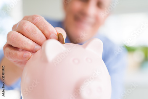 Man putting a coin inside piggy bank as savings smiling confident