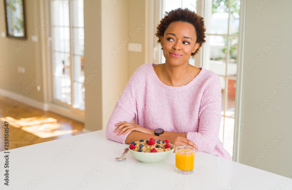 Young african american woman having healthy breakfast in the morning at home smiling looking side and staring away thinking.