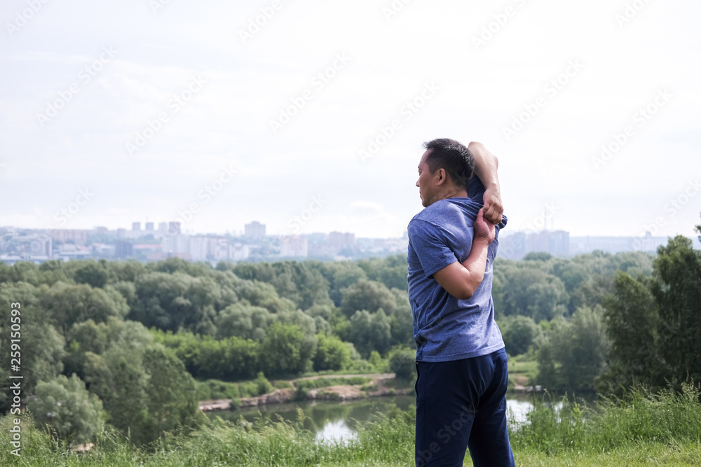 Korean man stretches against the background of the city. Healthy lifestyle. Adult man practicing yoga in nature. Korean man stretches against the background of the city. Healthy lifestyle. Adult man practicing yoga in nature.
