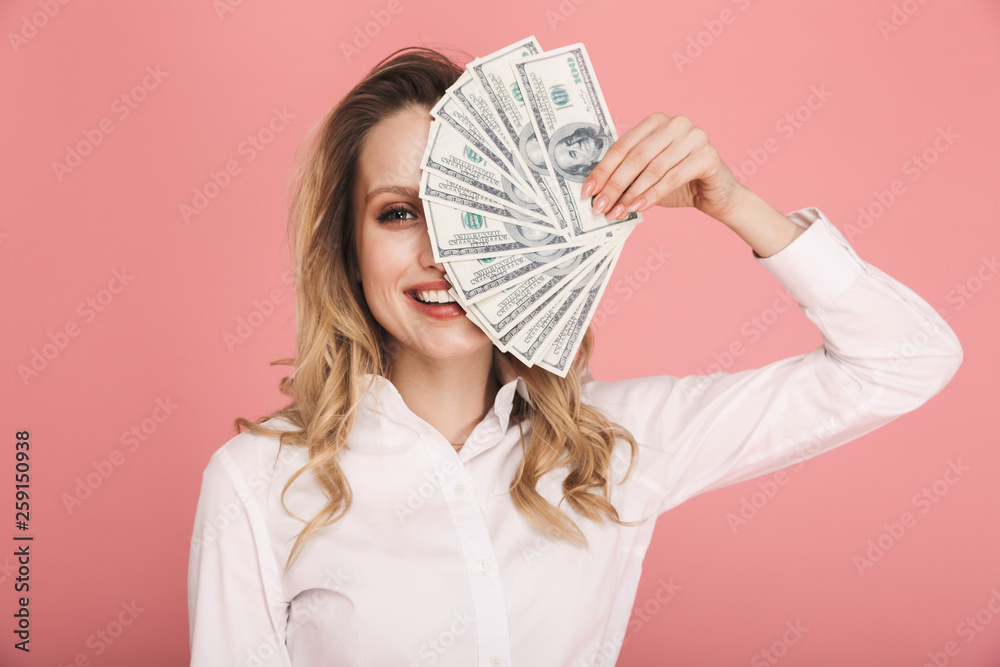 Portrait of gorgeous woman smiling and holding money fan isolated over pink background Portrait of gorgeous woman smiling and holding money fan isolated over pink background