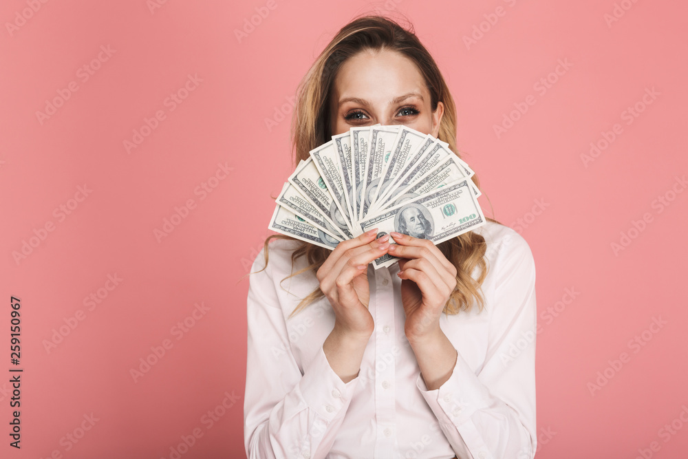 Portrait of stylish woman hiding while holding money fan isolated over pink background Portrait of stylish woman hiding while holding money fan isolated over pink background