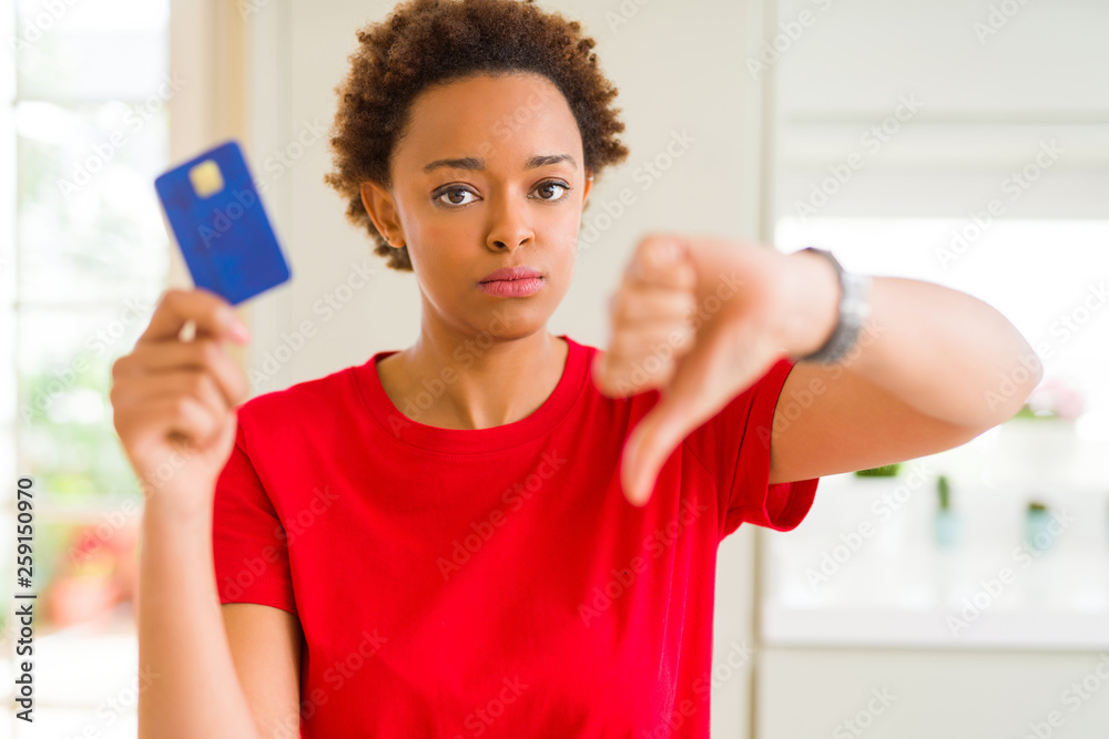Young african american woman holding credit card with angry face, negative sign showing dislike with thumbs down, rejection concept Young african american woman holding credit card with angry face, negative sign showing dislike with thumbs down, rejection concept