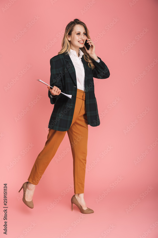Photo of attractive businesswoman wearing jacket holding clipboard and talking on cell phone Photo of attractive businesswoman wearing jacket holding clipboard and talking on cell phone