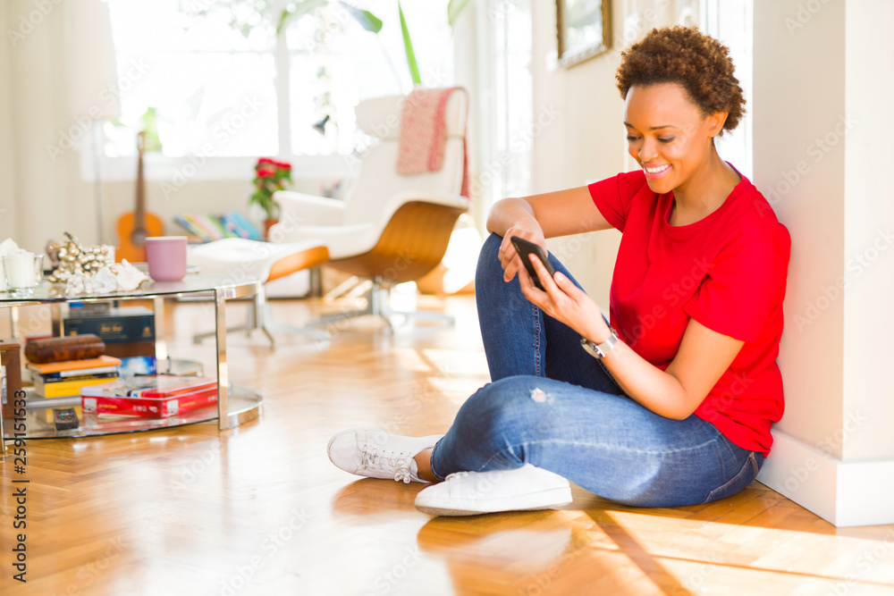 Beautiful young african american woman sitting on the floor using smartphone smiling