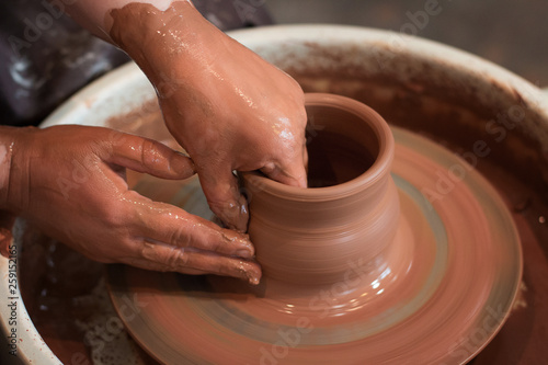 Rotating potter's wheel and clay ware on it taken from above. A sculpts his hands with a clay cup on a potter's wheel. Hands in clay. 