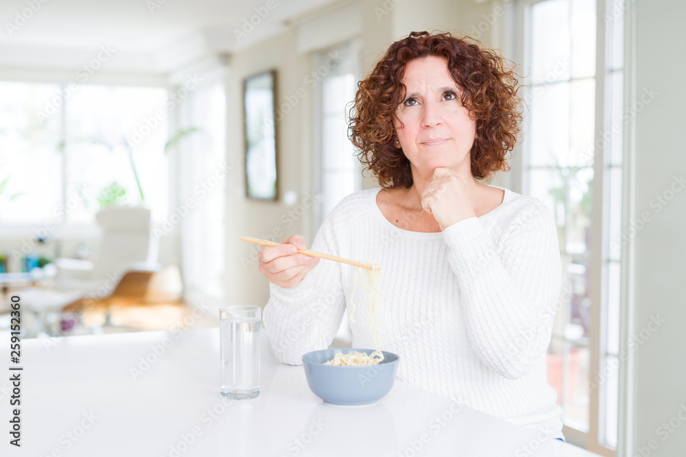 Senior woman eating asian noodles using chopsticks serious face thinking about question, very confused idea