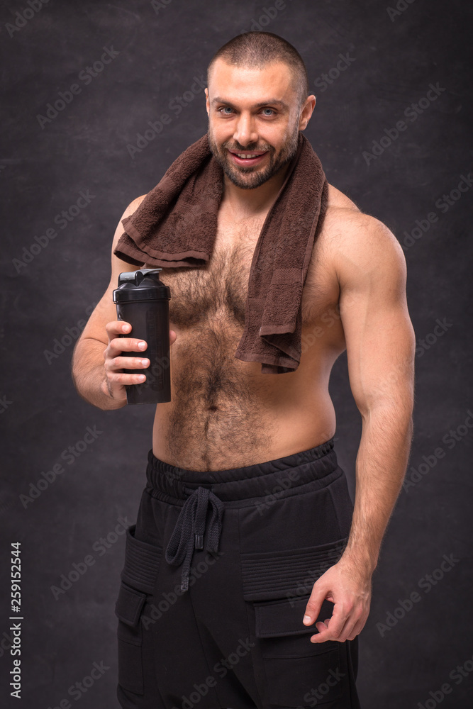 Young muscular bodybuilder man resting after a hard workout training, posing with a towel and shaker on black background Young muscular bodybuilder man resting after a hard workout training, posing with a towel and shaker on black background