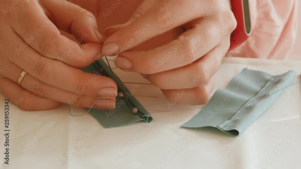 Seamstress at work with pins prepares a piece of blue fabric for sewing on the table in the workshop close-up Seamstress at work with pins prepares a piece of blue fabric for sewing on the table in the workshop close-up