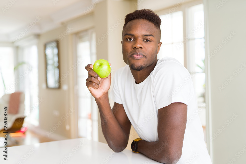 Young african american man eating fresh green apple with a confident expression on smart face thinking serious Young african american man eating fresh green apple with a confident expression on smart face thinking serious