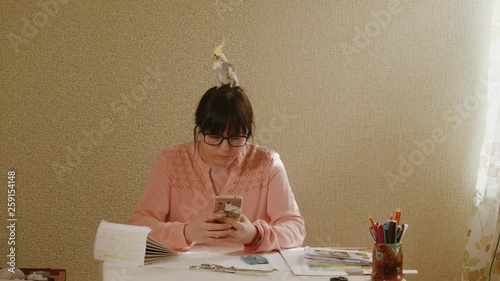 young girl with a parrot karella on his head looking at the smartphone photo