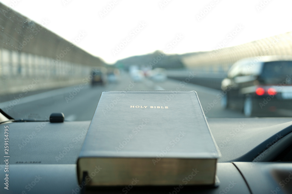 Holy Bible closed inside the car. blurred background highway with cars. White sky without clouds. Holy Bible closed inside the car. blurred background highway with cars. White sky without clouds.