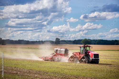 Agricultural background with red tractor pulling plow, throwing dust in air. Combine harvester at wheat field. Heavy machinery during cultivation, working on fields. Dramatic sky, rain, storm clouds
