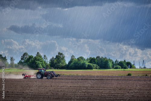 Agricultural background with tractor pulling plow, throwing dust in air. Combine harvester at wheat field. Heavy machinery during cultivation, working on fields. Dramatic sky, rain, storm clouds
