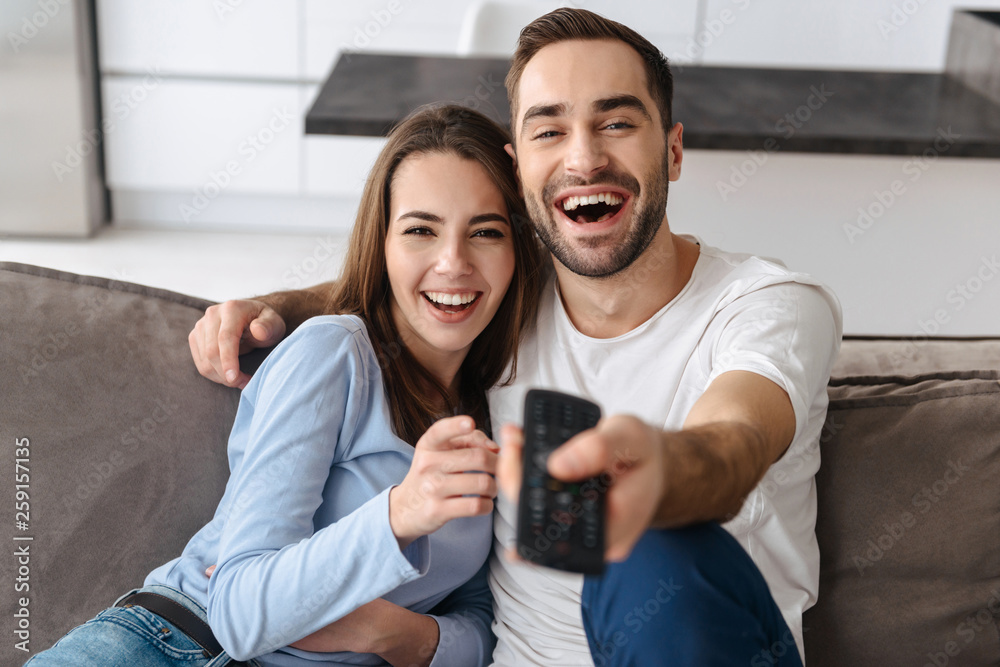 Fototapeta premium Image of happy couple holding remote control while watching television in living room