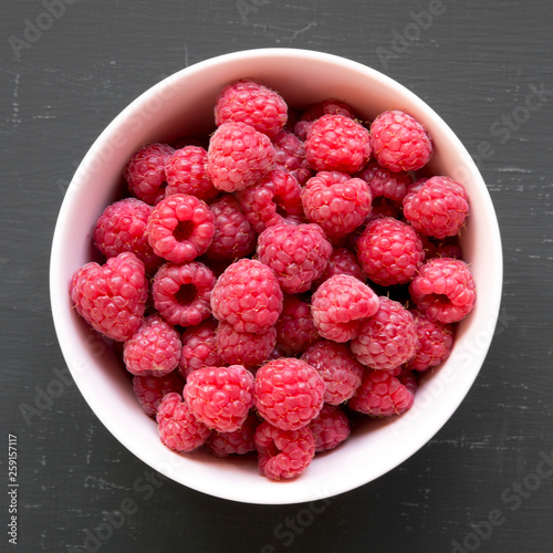 Pink bowl of raspberry on black surface, top view. From above, overhead. Close-up.
