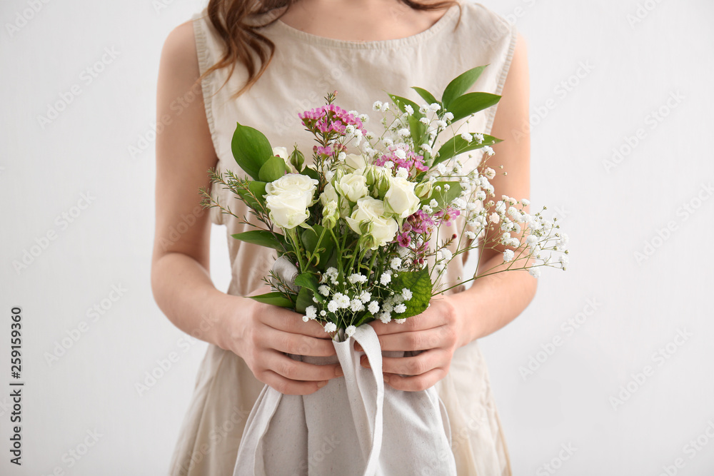 Young woman with bouquet of flowers in eco bag on light background