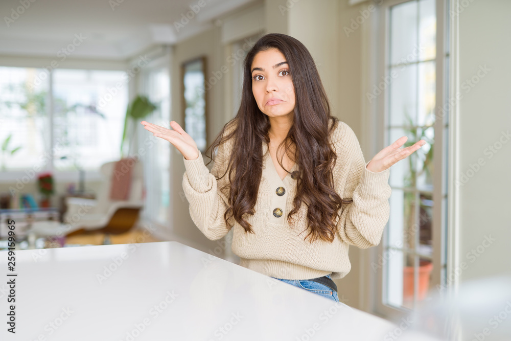 Young beautiful woman at home clueless and confused expression with arms and hands raised. Doubt concept. Young beautiful woman at home clueless and confused expression with arms and hands raised. Doubt concept.