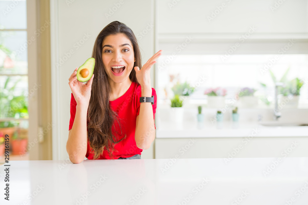 Young woman eating healthy avocado very happy and excited, winner expression celebrating victory screaming with big smile and raised hands Young woman eating healthy avocado very happy and excited, winner expression celebrating victory screaming with big smile and raised hands