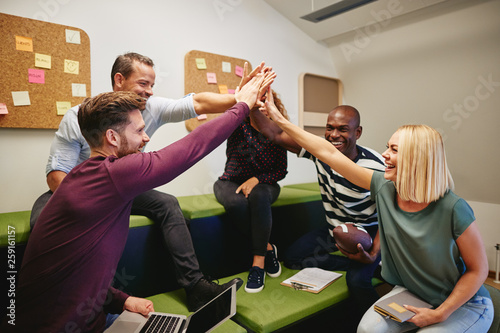 Laughing group of designers high fiving during an office meeting photo