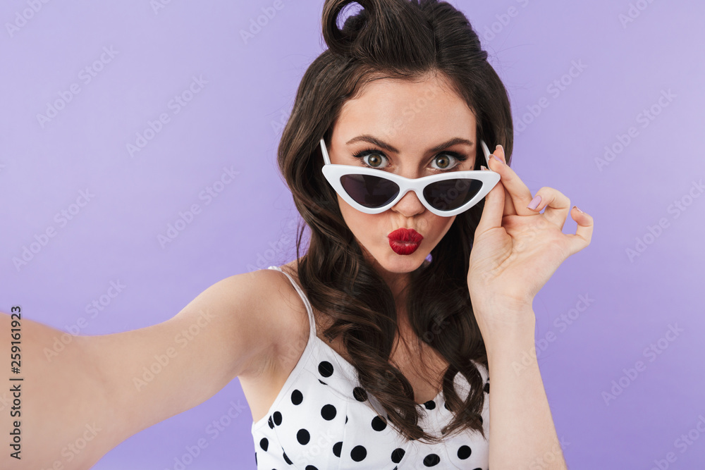 Portrait of beautiful pin-up woman 20s in vintage polka dot dress and retro sunglasses smiling at camera Portrait of beautiful pin-up woman 20s in vintage polka dot dress and retro sunglasses smiling at camera