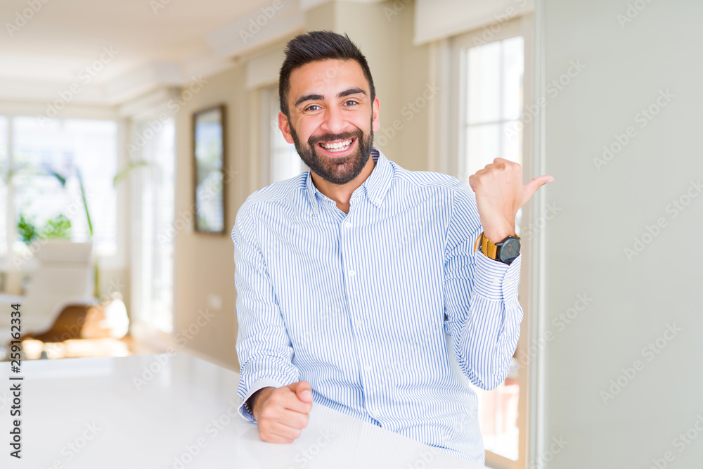 Handsome hispanic business man smiling with happy face looking and pointing to the side with thumb up. Handsome hispanic business man smiling with happy face looking and pointing to the side with thumb up.