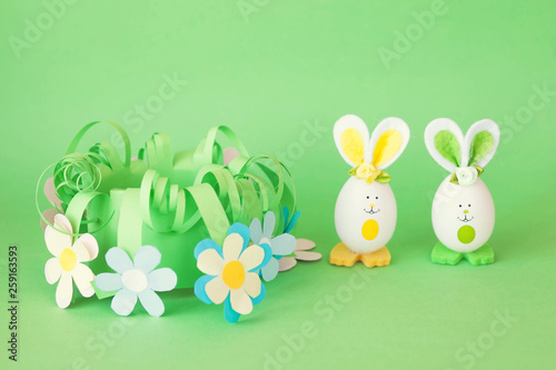 Easter holiday concept with cute handmade funny eggs bunny  in a homemade paper flower basket with a greeting text