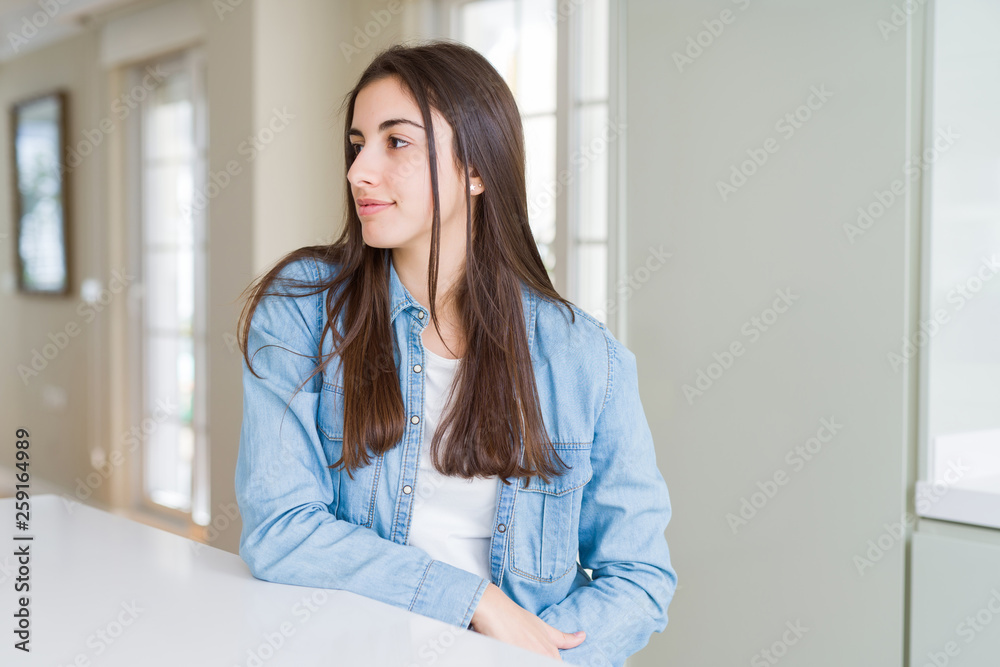 Beautiful young woman sitting on white table at home looking to side, relax profile pose with natural face with confident smile. Beautiful young woman sitting on white table at home looking to side, relax profile pose with natural face with confident smile.