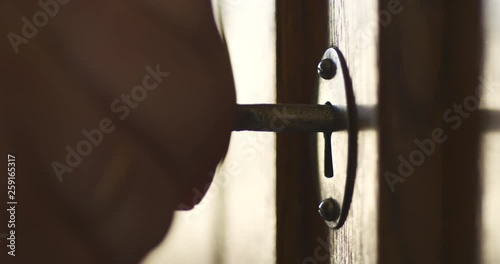 Side wiev of person by hand turns old key in the keyhole of antique wooden cabinet