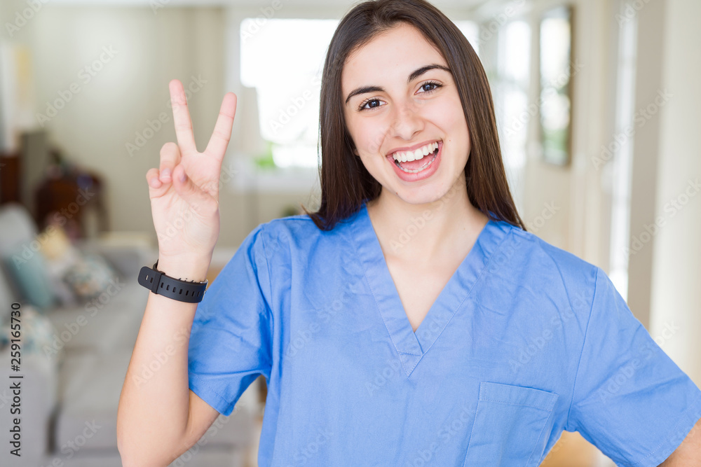 Beautiful young nurse woman at the clinic smiling with happy face winking at the camera doing victory sign. Number two. Beautiful young nurse woman at the clinic smiling with happy face winking at the camera doing victory sign. Number two.