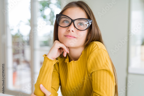 Beautiful young girl kid wearing glasses with hand on chin thinking about question, pensive expression. Smiling with thoughtful face. Doubt concept.