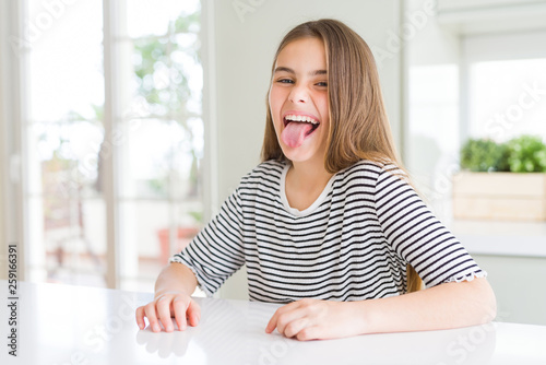 Beautiful young girl kid wearing stripes t-shirt sticking tongue out happy with funny expression. Emotion concept.