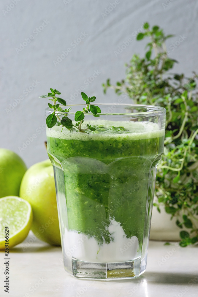 Green spinach kale apple honey smoothie in glass on white marble table with blender and ingredients above. Healthy organic eating.