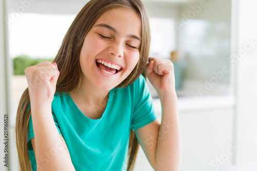 Beautiful young girl kid wearing green t-shirt excited for success with arms raised celebrating victory smiling. Winner concept.