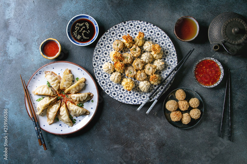 Dim sum Gyozas asian fried dumplings party set with variety of sauces served in ceramic plates and bowls with chopsticks, tea cups and teapot over dark blue texture background. Flat lay, space