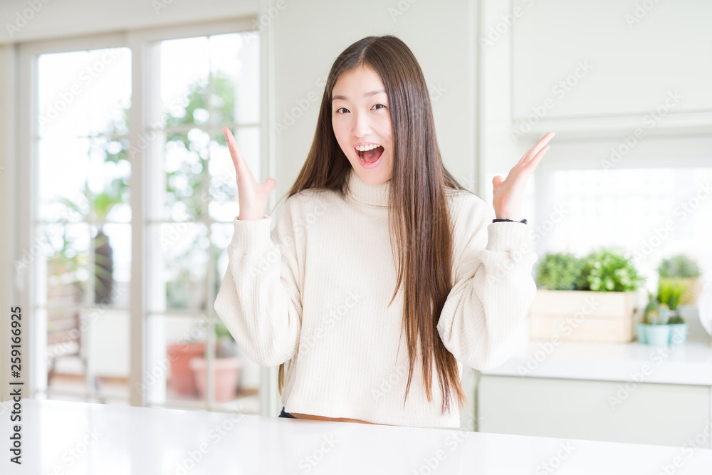 Beautiful Asian woman wearing casual sweater celebrating crazy and amazed for success with arms raised and open eyes screaming excited. Winner concept Beautiful Asian woman wearing casual sweater celebrating crazy and amazed for success with arms raised and open eyes screaming excited. Winner concept