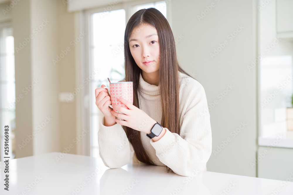 Beautiful Asian woman drinking a cup of coffee with a confident expression on smart face thinking serious Beautiful Asian woman drinking a cup of coffee with a confident expression on smart face thinking serious